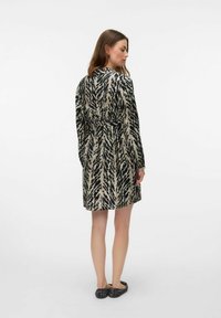 Robe à manches longues beige avec un motif abstrait noir, cintrée à la taille et d'une coupe droite. Associée à des ballerines noires texturées.