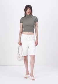 Olivenfarbendes, geripptes Kurzarmoberteil, weiße Denim-Shorts, beigen Rutschpantoletten und eine kleine weiße Handtasche. Minimalistisches Design mit einer figurnahen Silhouette.