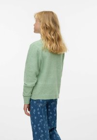 Roheline kudumipullover pika varrukaga ja soonikuga manšettide ning siniste ja valgete lillemustriga teksadega. Pehme tekstuur, mugav lõige.