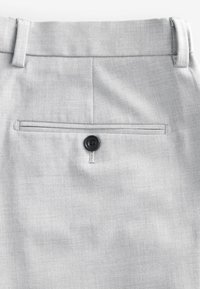 Pantaloni grigi chiari realizzati in tessuto strutturato, con una tasca posteriore dotata di un bottone nero e una cintura pulita e sagomata.