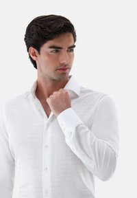 Camicia bianca con bottoni realizzata in tessuto testurizzato, colletto classico e polsini con bottoni. La camicia ha una vestibilità slim e sottili righe orizzontali.
