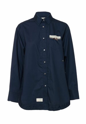 Tumesinist nuppudega särki kandes on kerge kangas, millel on pitsist ja paelast detail rinnataskul ning voltidega äärega.