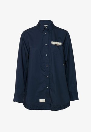 Tumesinist nuppudega särki kandes on kerge kangas, millel on pitsist ja paelast detail rinnataskul ning voltidega äärega.