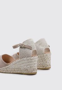 Sandalias de cuña de esparto beige con acentos de tejido trenzado, plantilla acolchada y correa en el tobillo, que presentan una plataforma de yute texturizada.