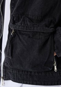Chaqueta de mezclilla negra con cremallera en el frente, bolsillos laterales y un acabado texturizado. Presenta detalles cosidos y un cordón ajustable en el dobladillo.
