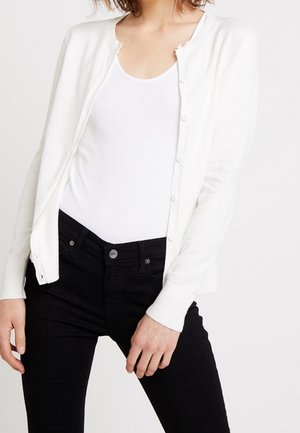 Witte cardigan, lichte brei, ronde halslijn, volledige knoopsluiting aan de voorkant, geribbeld textuur, gedragen over een aansluitend wit tanktop en zwarte jeans.