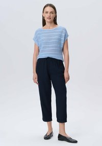 Jasnoniebieski sweter z krótkimi rękawami, w połączeniu z granatowymi spodniami na sznurek i czarnymi butami wsuwanymi. Prosty design, teksturowany materiał.