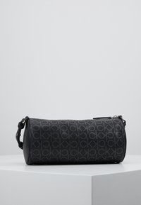 Borsa cilindrica nera in materiale testurizzato, con motivo a logo in rilievo, tracolla regolabile e chiusura con cerniera.