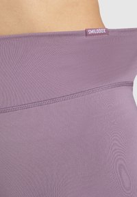 Leggings high-waisted di un delicato lavanda realizzati in un tessuto elasticizzato, caratterizzati da una texture liscia e un piccolo tag "SMILODOX" sulla vita.