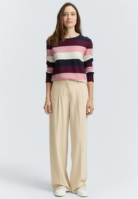 Pull rayé dans des tons riches de rose, marine et crème, associé à un pantalon large beige et des baskets blanches, présentant une coupe décontractée et une texture douce.