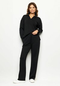 Completo sportivo nero composto da una maglia a maniche lunghe e scollatura a V, abbinata a pantaloni coordinati, completato da sneakers bianche.