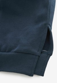 Granatowa bluza z prążkowanymi mankietami, z bocznymi rozcięciami na dole. Gładka faktura, materiał z mieszanki bawełny oraz przeszycia.