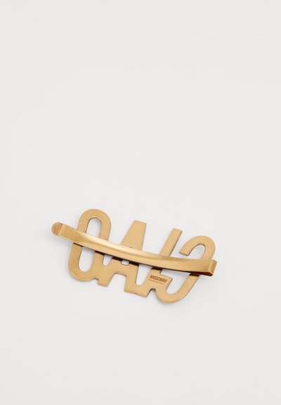 Gold-tone hair clip featuring an abstract design with cut-out letters. Smooth texture with a shiny finish and a curved holding bar.