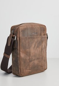 Braune Leder-Umhängetasche mit rechteckiger Form, Reißverschluss und verstellbarem Schultergurt. Verfügt über gestickte Akzente und ein Logo.