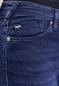 Jeans in denim blu scuro con vita media, tasche frontali, bottone in metallo e cuciture tonali. Accento del logo sulla tasca.