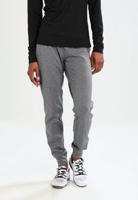 Szare spodnie dresowe z miękkiego materiału, z elastycznym pasem i mankietami, w połączeniu z białymi butami sportowymi. Widoczna czarna bluzka z długim rękawem.