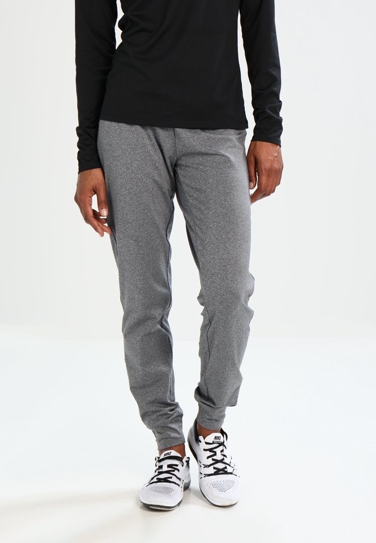 Szare spodnie dresowe z miękkiego materiału, z elastycznym pasem i mankietami, w połączeniu z białymi butami sportowymi. Widoczna czarna bluzka z długim rękawem.