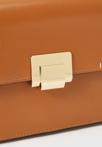 Sac à main en cuir marron avec une texture lisse et une forme rectangulaire. Présente un fermoir doré et des détails de couture subtils.