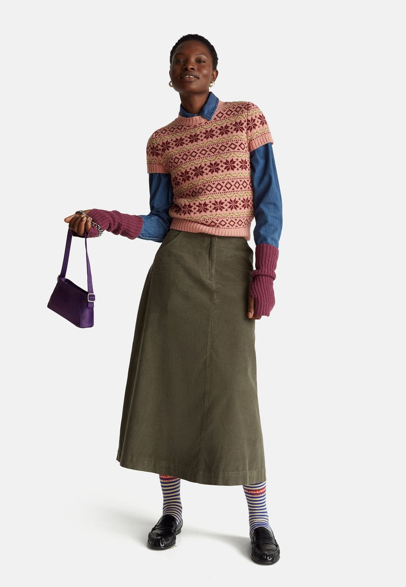 Růžový pletený svetr s květinovými vzory, nošený přes džínovou košili. Olivově zelená sukně, pruhované ponožky, černé mokasíny a malá fialová kabelka.