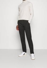 Grau karierte Hose mit maßgeschneidertem Schnitt, aus einem glatten Stoff, kombiniert mit einem hellen creamfarbenen Rollkragenpullover und weißen Sneakers.