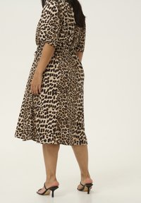 Leopardenmuster Midi-Kleid mit kurzen Ärmeln, tailliertem Schnitt, fließendem Rock und glattem Stoff. Schwarze High Heels runden das Outfit ab.