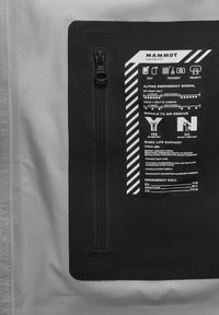 Schwarzes Stoffpanel mit einem Reißverschluss, das weiße gedruckte Notfallanweisungen und Symbole auf einem grauen Hintergrund enthält.