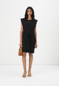 Black short dress with a relaxed fit, featuring lace trim on sleeves and a drawstring waist. Paired with a tan handbag and strappy sandals.