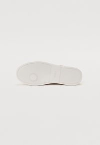 Suola di sneaker bianca con gomma testurizzata per la presa, caratterizzata da un accento circolare e un sottile logo del marchio. Design pulito con dettagli minimi.