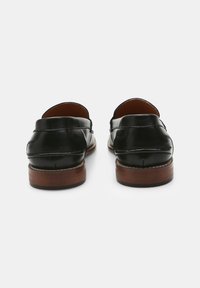 Mocasines de cuero negro con puntera redondeada, tacón ligeramente elevado, detalles de costura sutiles y textura suave.