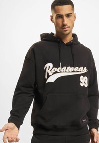 Fekete kapucnis pulcsi pamutkeverékből, elöl fehér "Rocawear" logóval és "99" felirattal, kenguru zsebbel és bordázott mandzsettával.