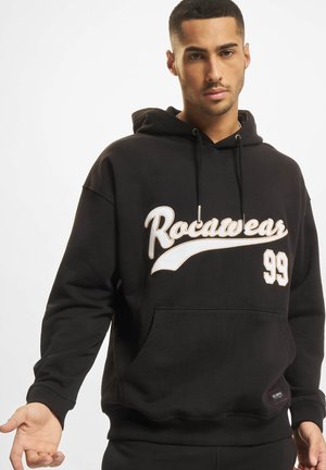 Svart hettegenser laget av bomullsblanding med en hvit "Rocawear"-logo og "99" trykket på fronten, med kengurulomme og ribbede mansjetter.