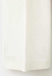 Gros plan de l'ourlet inférieur d'un pantalon en tissu blanc montrant des coutures visibles et une couture droite.