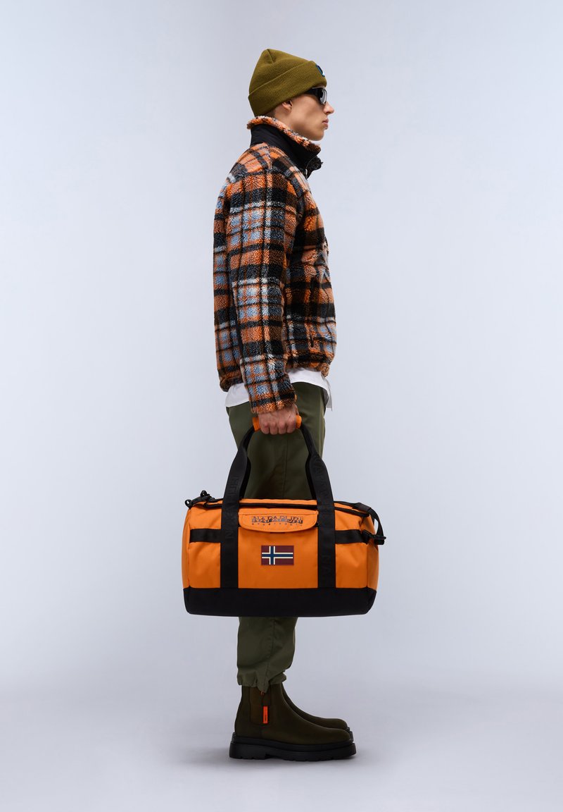 Bolsa de deporte naranja y negra con un parche de bandera, asas resistentes y una parte superior con cremallera. La tela de la bolsa parece duradera y resistente al agua.