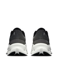 Scarpe sportive nere e grigie con una parte superiore testurizzata e una suola intermedia bianca. Presentano un design della suola distintivo con aperture per una maggiore flessibilità.