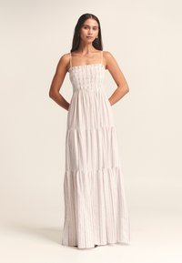 Vestido largo en blanco con sutiles rayas verticales en rojo y azul. Cuenta con un cuerpo fruncido y una falda de capas con un ajuste relajado.