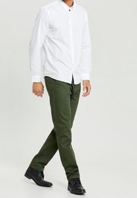 Chemise blanche à manches longues avec des boutons, pantalon slim vert et chaussures de ville noires. Design simple et classique avec des lignes épurées et sans motifs.