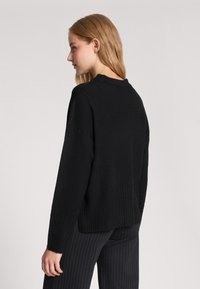 Czarny sweter dzianinowy o prążkowanej fakturze, okrągłym dekolcie i opadających ramionach, zestawiony z spodniami w paski. Prosty i wszechstronny design.