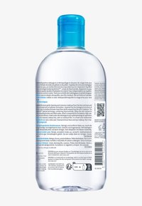 Transparente Plastikflasche mit blauem Verschluss. Auf der Rückseite befindet sich Text in mehreren Sprachen, der Informationen zur Produktanwendung und zu den Inhaltsstoffen enthält.