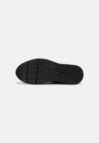 Semelle de sneaker noire avec des rainures texturées et un motif de semelle pour l'adhérence, avec un logo surélevé près du talon.