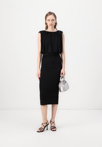 Black sleeveless top with gathered neckline, paired with a form-fitting black midi skirt. Accessories include a silver handbag and black strappy heels.