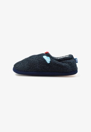 Zapatilla borrosa azul marino con suela plana, un pequeño broche rojo en la parte superior y un logotipo bordado en azul claro en el lateral.