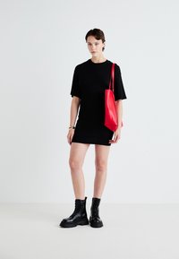 Melnas īsām piedurknēm kleita ar pieguļošu siluetu, apvienota ar spilgti sarkanu ādas rokassomu un melniem šņorējamiem potīšu zābakiem.