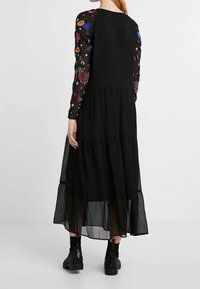 Schwarzes Kleid mit langen, durchsichtigen bestickten Ärmeln, die farbenfrohe Blumenmuster zeigen, gestuftem Rockdesign und fließender Silhouette.