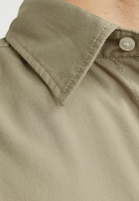 Camisa de cuello en tejido caqui, con cierre de botón, textura suave y costuras bien cosidas. Acercamiento al cuello y la tela.