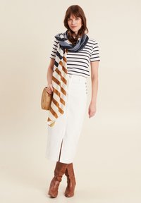 Jupe en denim blanc avec une fente à l'avant et des détails de boutons, associée à un t-shirt rayé bleu marine et blanc et un foulard à motifs. Bottes marron jusqu'aux genoux.