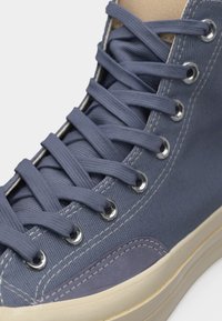 Μπλε καμβάς αθλητικό παπούτσι με ψηλή γλώσσα, μπλε κορδόνια που ταιριάζουν, μεταλλικά ροδέλες, λευκή ραφή και εκρού καουτσούκ σόλα.