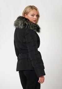 Juodas pūkinis parkas su dirbtiniu kailiu kaklo apdailai, įvertintas liemuo ir horizontalių siūlių detalės. Lygus tekstūra ir prigludusi siluetas.