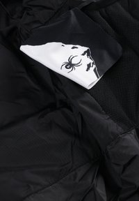 Giacca nera con un esterno in nylon liscio. Un fazzoletto bianco con una grafica di ragno contrasta con l'interno in tessuto a rete nera.