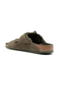 Pantofola scivolosa in suede marrone con fodera in pelliccia, soletta in sughero, suola in gomma e design aperto. Presenta una branding minimale sul lato.
