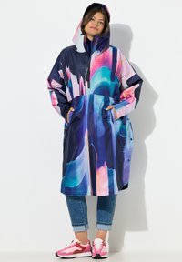 Langer Regenmantel mit Kapuze, versehen mit einem mehrfarbigen abstrakten Muster in Blau, Pink und Lila. Hergestellt aus glänzendem wasserdichtem Material.